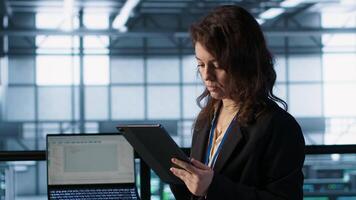 Technician in data center with tablet integrating AI driven automation tools, running predictive maintenance routines. Woman ensuring continuous uptime of server room, managing data flows, camera A video