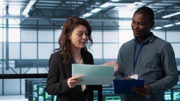 IT professionals in data center reviewing reports and files, crosschecking network performance metrics and security logs. Server room workers doing troubleshooting to prevent downtime, camera A video