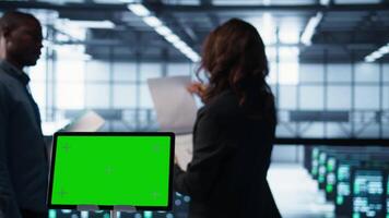 Close up of chroma key tablet next to server room data scientists conducting security audits, preventing bugs. Green screen device and man working with colleague in data center, camera B video