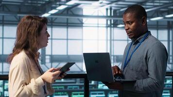 System administrators using notebook device in data center, managing server virtualization. IT specialists using laptop in server farm, sustaining long term infrastructure reliability, camera A video