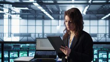 Admin in data center using artificial intelligence tech on tablet to deploy new server architectures. Woman in server room updating storage arrays to maintain stable performance, camera B video