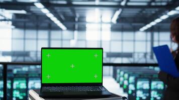 Green screen laptop in front of data center engineers in blurry background calibrating energy usage, inspecting servers configuration, supporting sustainable infrastructure, camera B video