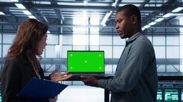 Technicians in data center using green screen mockup laptop to develop disaster recovery plans. IT specialists in server farm testing failover scenarios on chroma key device, protecting data, camera B video