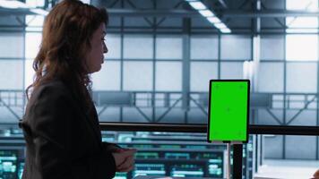 Programmers in data center brainstorming, using mockup tablet, observing equipment analytics. Server hub IT coworkers use isolated screen device, adjusting system parameters, camera A video