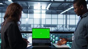 Data center system administrators using mockup laptop to review equipment diagnostics. Teamworking IT specialists adjusting server farm configurations using chroma key notebook video