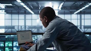 Technician in data center using laptop, adjusting power management settings, using programming languages. Man in server room optimizes resource utilization, maintaining stable infrastructure, camera B video