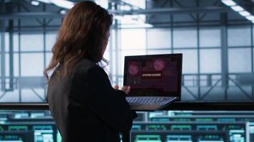 Cybersecurity expert in data center frantically trying to counter a hacker attack. Server room worker under pressure to secure sensitive information after threat alert received on laptop, camera A video