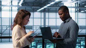 Developers in data center using laptop and tablet, executing security patches, securing firewall. Server farm workers using devices to perform vulnerability scans, ensuring data protection, camera A video