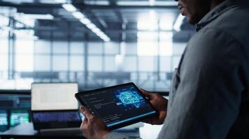 Close up of computer scientist in data center uses AI on tablet, verifying compliance of racks. IT expert using artificial intelligence on device to optimize resource utilization, camera B video