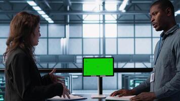 Engineers overseeing server room with mockup device, reading hardware documentation paperwork. Team doing inspection in server hub, reading technical files on green screen tablet, camera A video