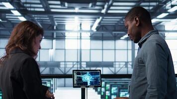 Team of IT professionals looking over data center checkup paperwork, using AI tech on tablet. Colleagues collaborating in server farm, reading documentation, using artificial intelligence, camera B video