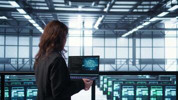AI technology used by data center software developers reviewing equipment diagnostics. Programmers coding on laptop using artificial intelligence, adjusting server farm configurations, camera B video
