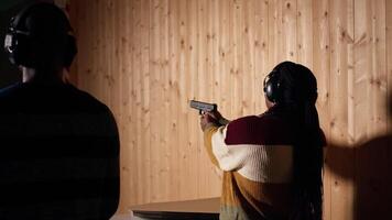 Woman in firing range training with pistol, looking at results on paper target. African american person doing shooting sport, sharpening skills, checking points scored on bullseye, camera A video