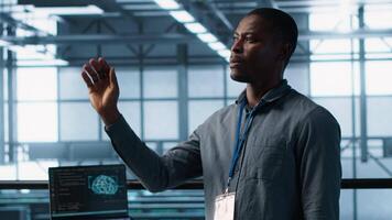 Computer scientist looking at holograms in data center, using artificial intelligence. African american admin interacting with augmented reality AI visualization in server hub, camera A video