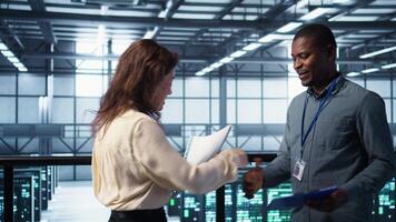 Data center engineer greeting colleague, examining system diagnostics paperwork together. Server room workers doing handshake, meeting to look over maintenance reports, camera B video