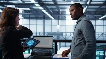 Teamworking data center computer scientists using artificial intelligence on laptop and tablet. Server room coworkers using neural networks AI on devices to do computing processes, camera B video