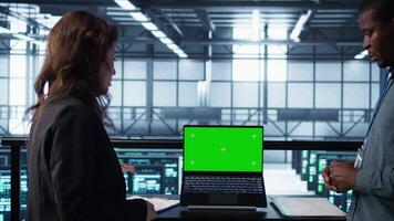 Coworkers in data center using mockup laptop, integrating green technologies. IT experts in server room using chroma key notebook to implement sustainable energy solutions, camera B close up video