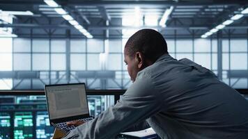 Technician coding on laptop in data center, managing server virtualization, finetuning network protocols. Server farm employee programming on notebook, enforcing advanced security measures, camera B video
