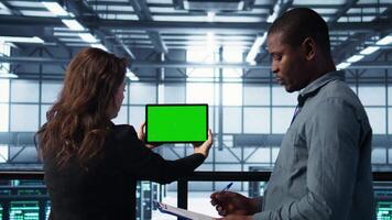 System administrators in server farm using isolated screen mockup tablet to verify settings. Data center colleagues using green screen chroma key device to monitor facility, camera B video