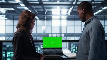 Data center team of computer scientists using mockup laptop to review equipment diagnostics. Teamworking IT experts adjusting server room configurations using chroma key notebook, camera B video
