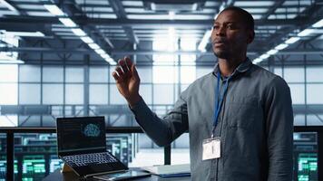 Computer scientist looking at holograms in data center, using artificial intelligence. African american admin interacting with augmented reality AI visualization in server hub, camera B video