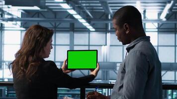 System administrators in server farm using isolated screen mockup tablet to verify settings. Data center colleagues using green screen chroma key device to monitor facility, camera A video