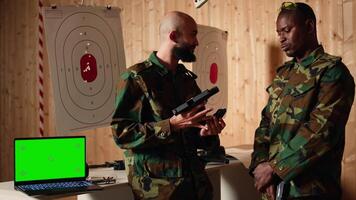 Green screen notebook next to army soldiers practicing with firearms in shooting range and having conversation. Chroma key laptop next to military units holding pistols talking, camera A video