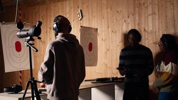 Firing range customer looking in zooming device to check if he shot bullseye next to instructor overseeing client. Person analyzing targets shot using magnifying lens during firearm practice, camera A video