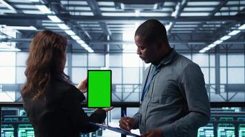 Engineers using green screen tablet in data center, checking infrastructure reliability, writing in clipboard. Workers using mockup device in server room, managing server virtualization, camera B video