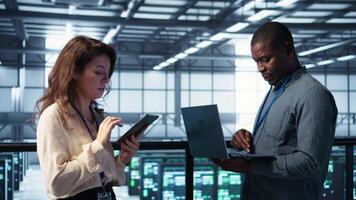 Colleagues in data center workplace use laptop to calibrate energy usage. Server farm IT specialist using notebook to inspect UPS configurations, doing maintenance on equipment, camera B video