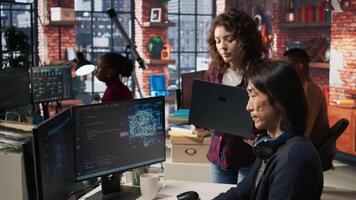 IT engineers cooperating in AI focused startup, debugging applications, crosschecking between PC and laptop. Coworkers doing code testing and quality assurance on devices, camera A video