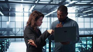 Developers in data center workspace coding on laptop, analyzing metrics, optimizing storage volumes. Teamworking IT professionals in server room using notebook, ensuring seamless operations, camera B video