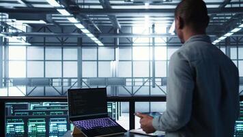 Technician in data center using AI on laptop and tablet, developing disaster recovery plans. Server farm employee using artificial intelligence tech on devices, testing failover scenarios, camera B video