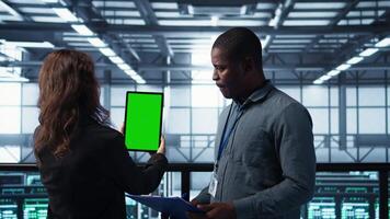 técnicos dentro dados Centro usando verde tela tábua, revendo hardware diagnósticos. isto colegas de trabalho ajustando servidor configurações usando brincar dispositivo, aplicando firmware atualizações, Câmera b video