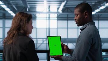 Server room data scientists using mockup tablet, conducting security audits to prevent bugs. African american man with colleague in data center looking at green screen device, camera A video