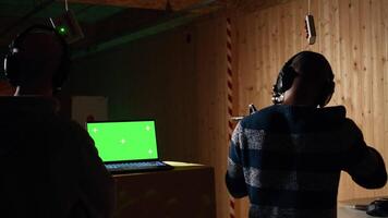 Green screen laptop in shooting range next to man successfully shooting targets. Mockup notebook next to person being congratulated by instructor for accurately hitting bullseye, camera A video