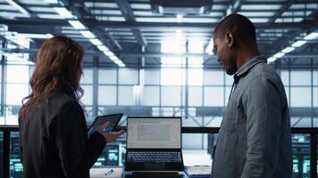 Programmers using AI technology on laptop and tablet in data center employing machine learning models. Devices used by artificial intelligence IT experts in server farm, camera B video
