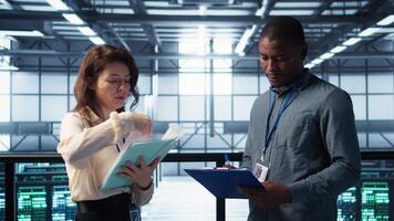 Data center team reviewing paperwork files in high tech server room, analyzing critical system reports and security protocols. Server room admins looking over financial documents, camera B video