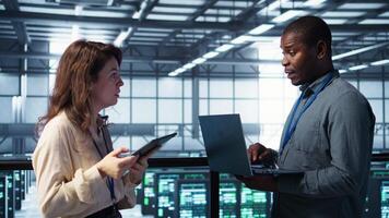 System administrators using notebook device in data center, managing server virtualization. IT specialists using laptop in server farm, sustaining long term infrastructure reliability, camera B video