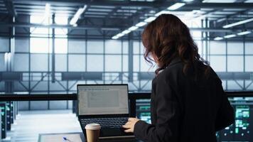 Programmer using laptop in data center, finetuning network protocols, drinking coffee. Woman in server farm coding on notebook, enjoying beverages, enforcing advanced security measures video