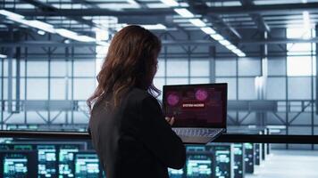 Cybersecurity expert in data center frantically trying to counter a hacker attack. Server room worker under pressure to secure sensitive information after threat alert received on laptop, camera B video