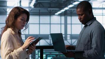 Portrait of happy system administrators in data center using devices, verifying firewall configurations. Jolly teamworking IT experts performing equipment vulnerability scans in server hub, camera A video