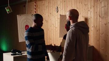 Shooting gallery worker meeting with customers, greeting them, demonstrating how to safely reload pistol. Firing range expert welcoming clients, doing hand shake, teaching weapon handling, camera A video