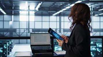 Technician in data center with tablet integrating AI driven automation tools, running predictive maintenance routines. Woman ensuring continuous uptime of server room, managing data flows, camera B video