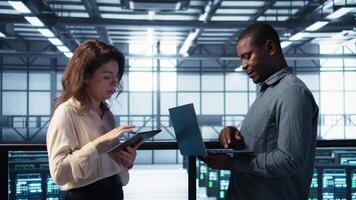 Developers in data center using laptop and tablet, executing security patches, securing firewall. Server farm workers using devices to perform vulnerability scans, ensuring data protection, camera B video