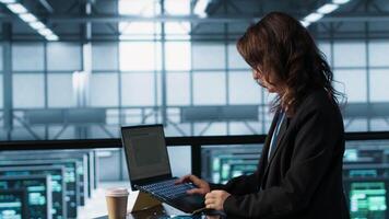 Admin in data center using laptop to update storage arrays, configuring network virtualization. Woman in server room holding coffee cup, verifying settings to maintain stable performance, camera A video