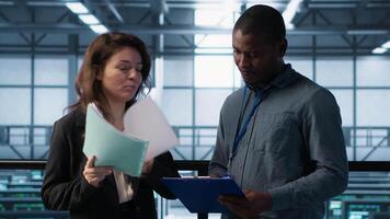 Data center management executives reading paperwork files, reviewing system diagnostics. Server farm colleagues looking over maintenance schedules documents and cybersecurity protocols, camera A video