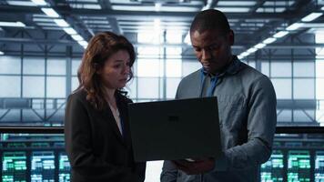 Engineers using laptop in data center, managing server virtualization, running scripts. IT specialists using programming language on notebook in server hub, finetuning network protocols, camera B video