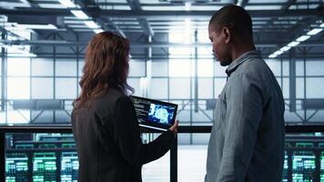 Data center technicians deploying AI driven management tools using tablet. Server farm coworkers inspecting server clusters, updating network topologies using artificial intelligence, camera B video