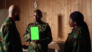 Team of military units at shooting range watching on green screen tablet to learn necessary combat skills. Army soldiers looking at instructions on chroma key device during training, camera A video